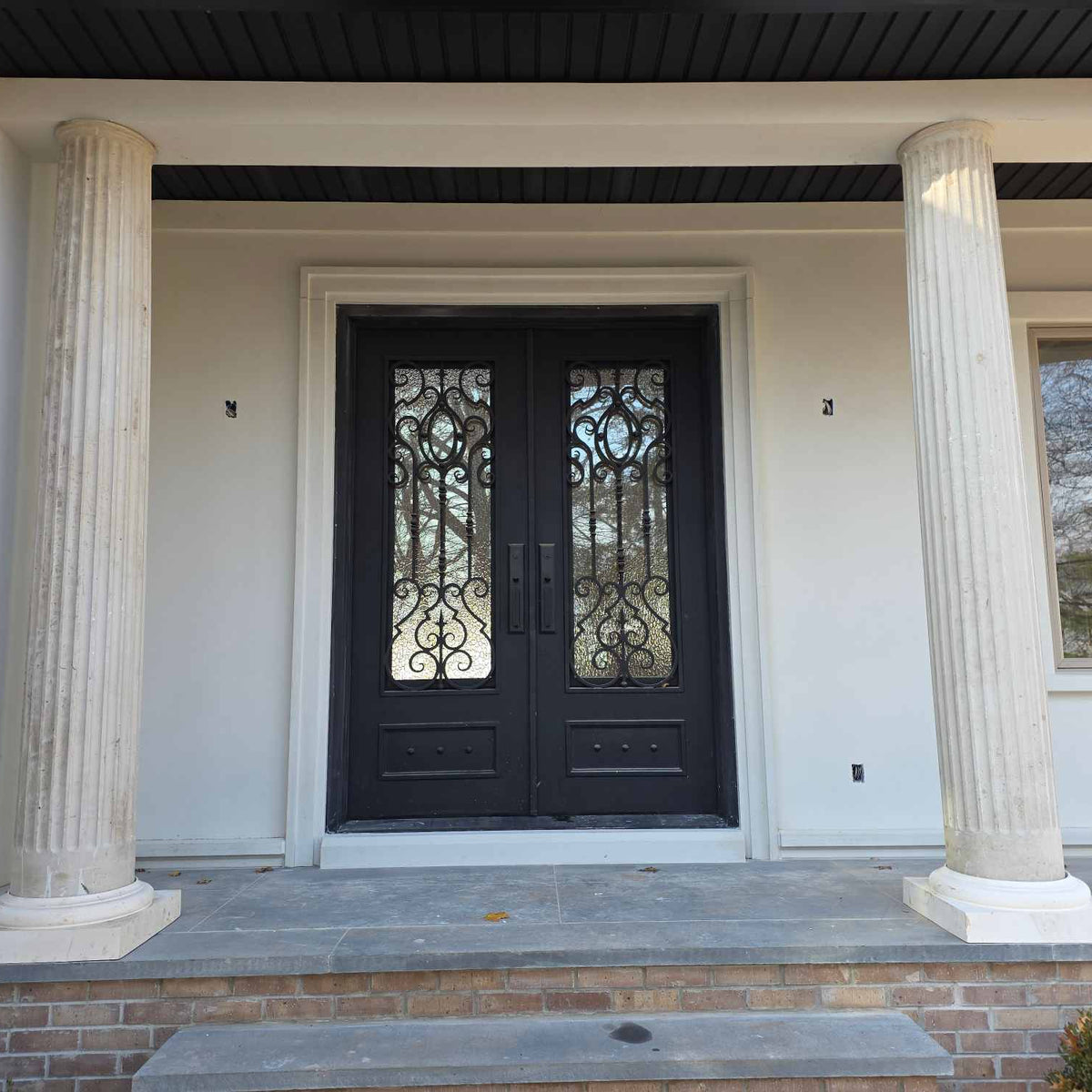 Front door of a house with decorative glass panels and flanked by columns.