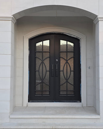 Black wrought iron door with decorative glass panels on a light stone building.