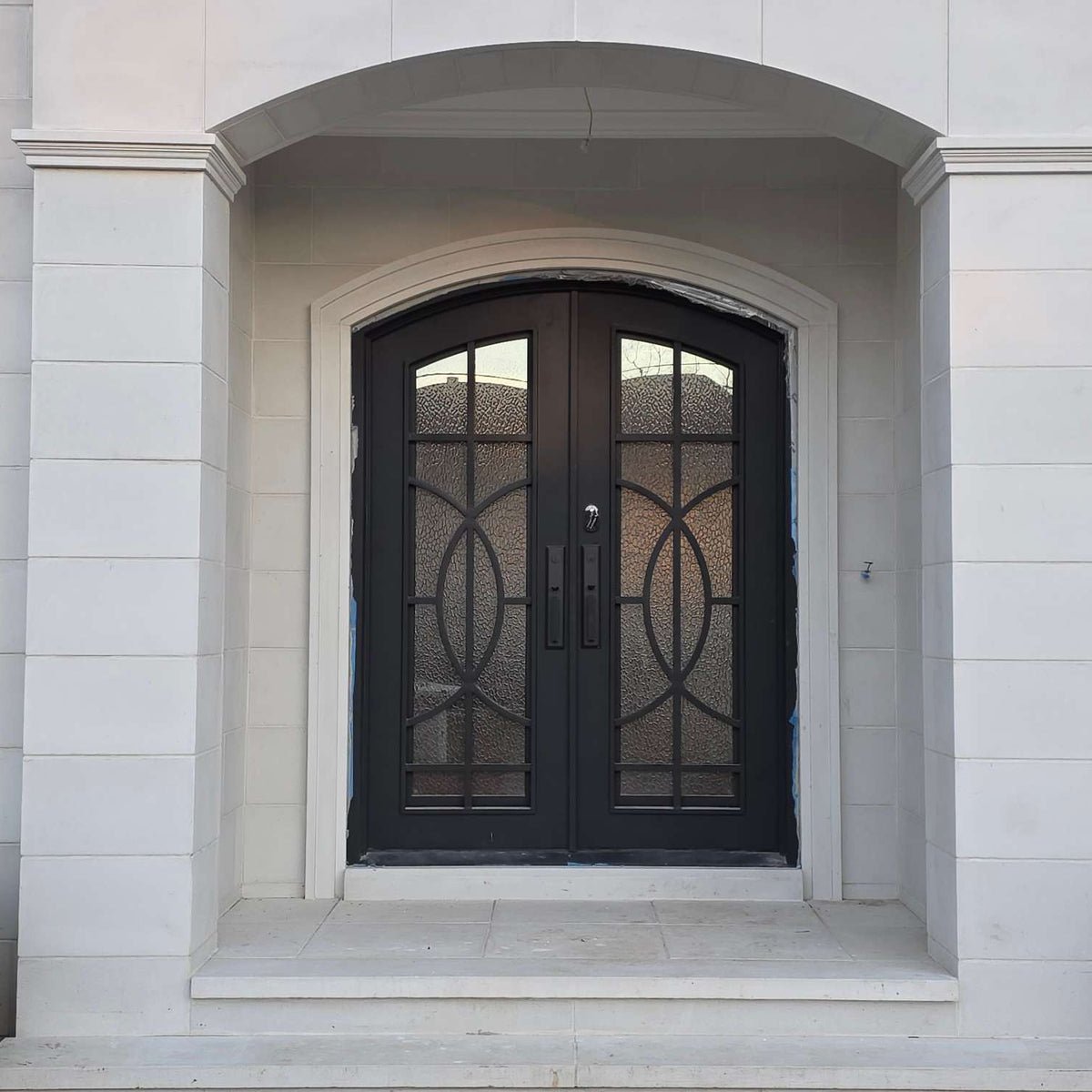 Black wrought iron door with decorative glass panels on a light stone building.